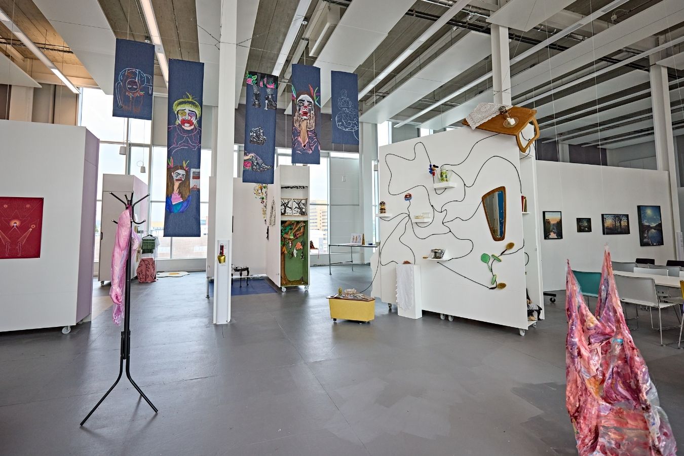 A view inside a modern building with artwork displayed on white walls and hung from the ceiling