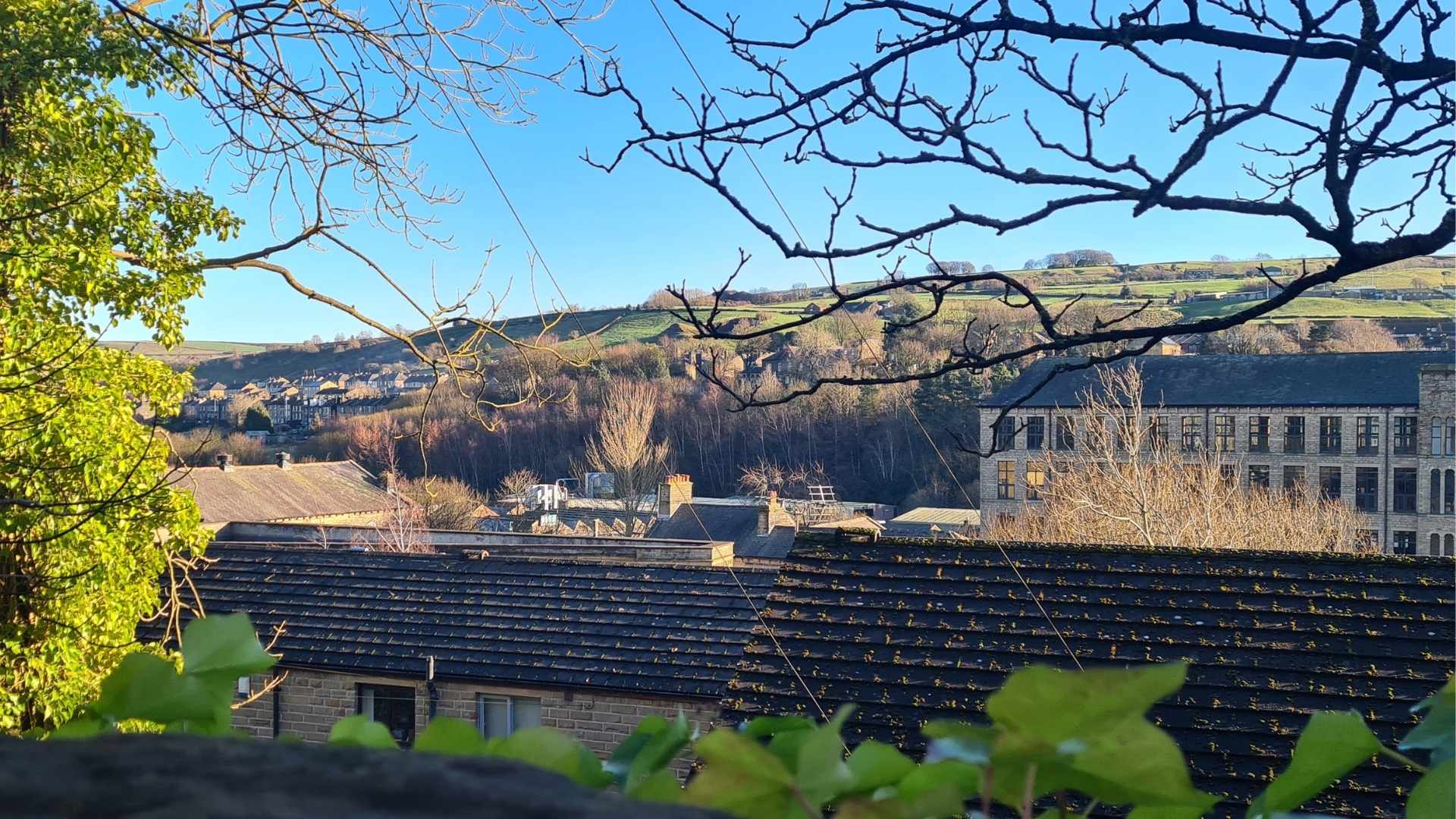 A view from a window with renovated industrial buildings in the foreground and hills and blue sky beyond